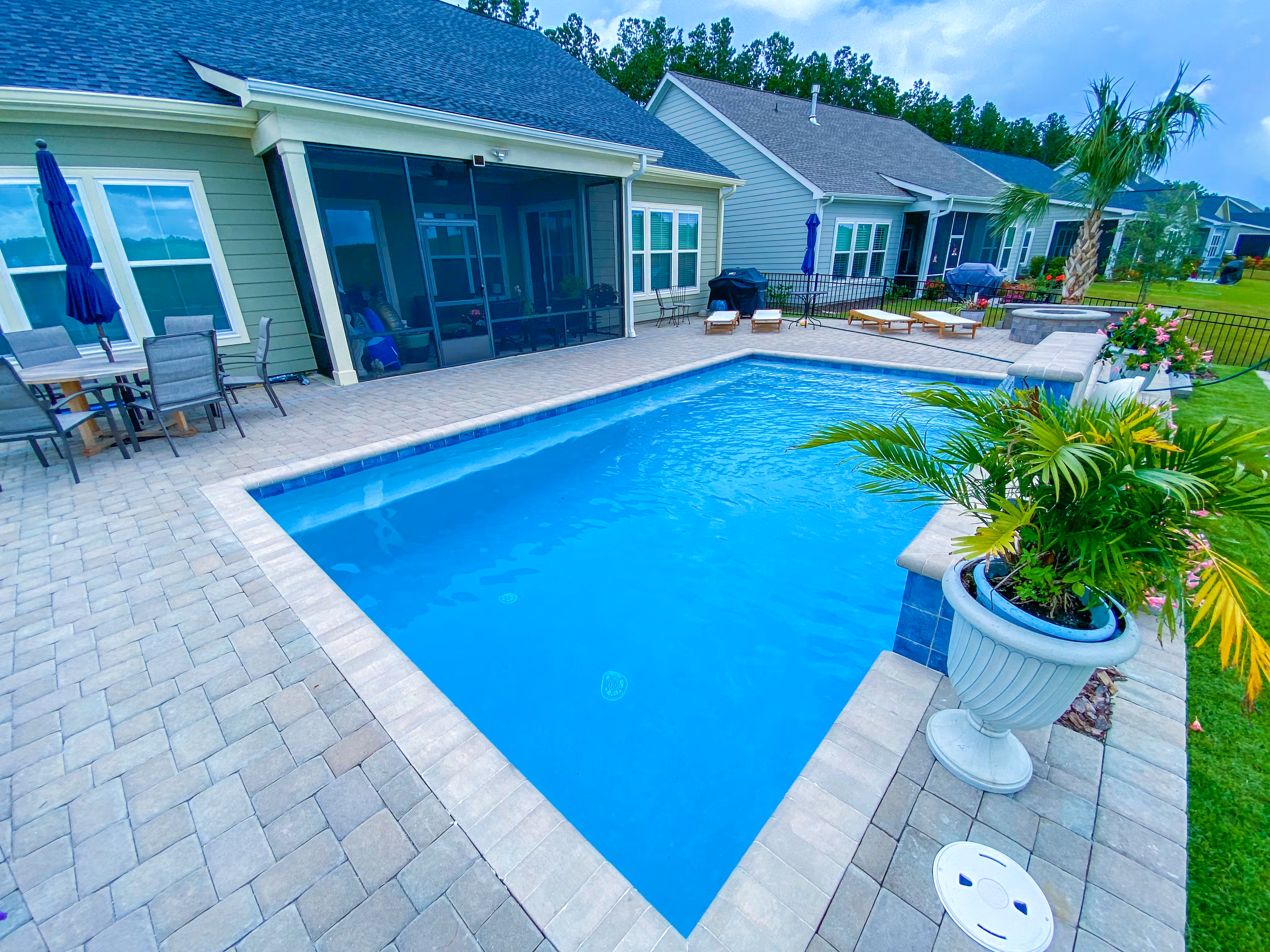A backyard pool with a tan stone paver deck.