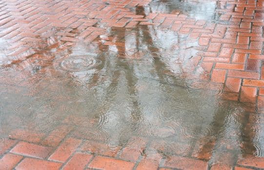 Rainwater pooling on a brick paver patio, highlighting poor drainage and standing water after a rainstorm.